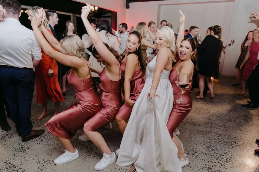 Bride and bridesmaids dancing together with their arms raised