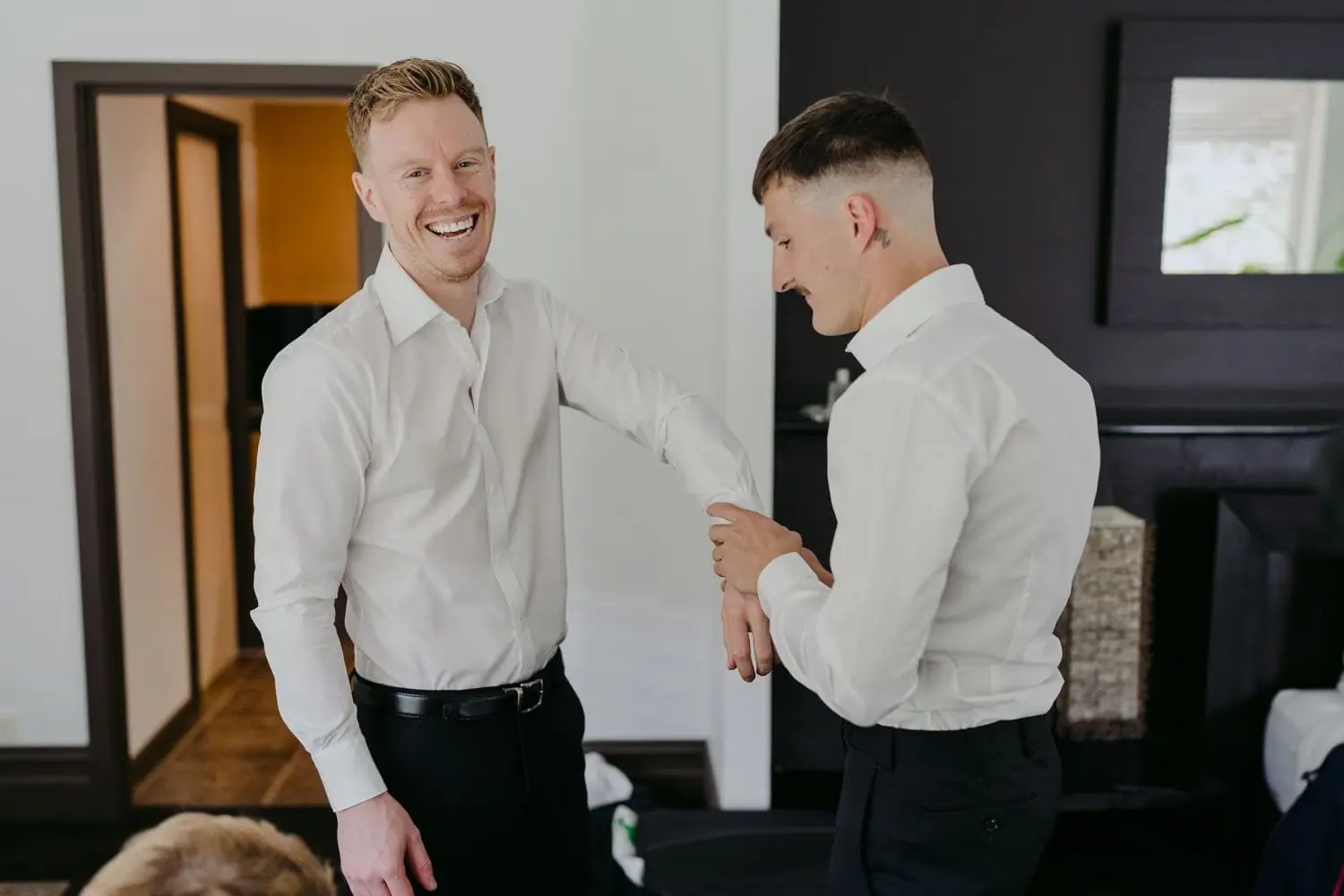 Groom laughing as a groomsman helps him adjust his shirt sleeve