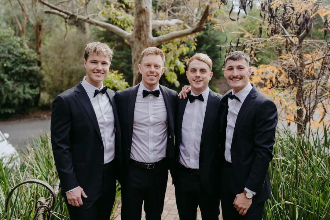 Groom and groomsmen standing together beside a garden pond