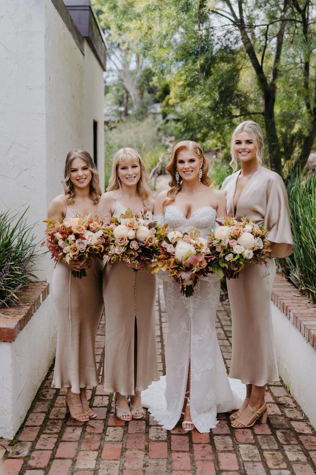Bride and bridesmaids holding bouquets beside a brick garden path