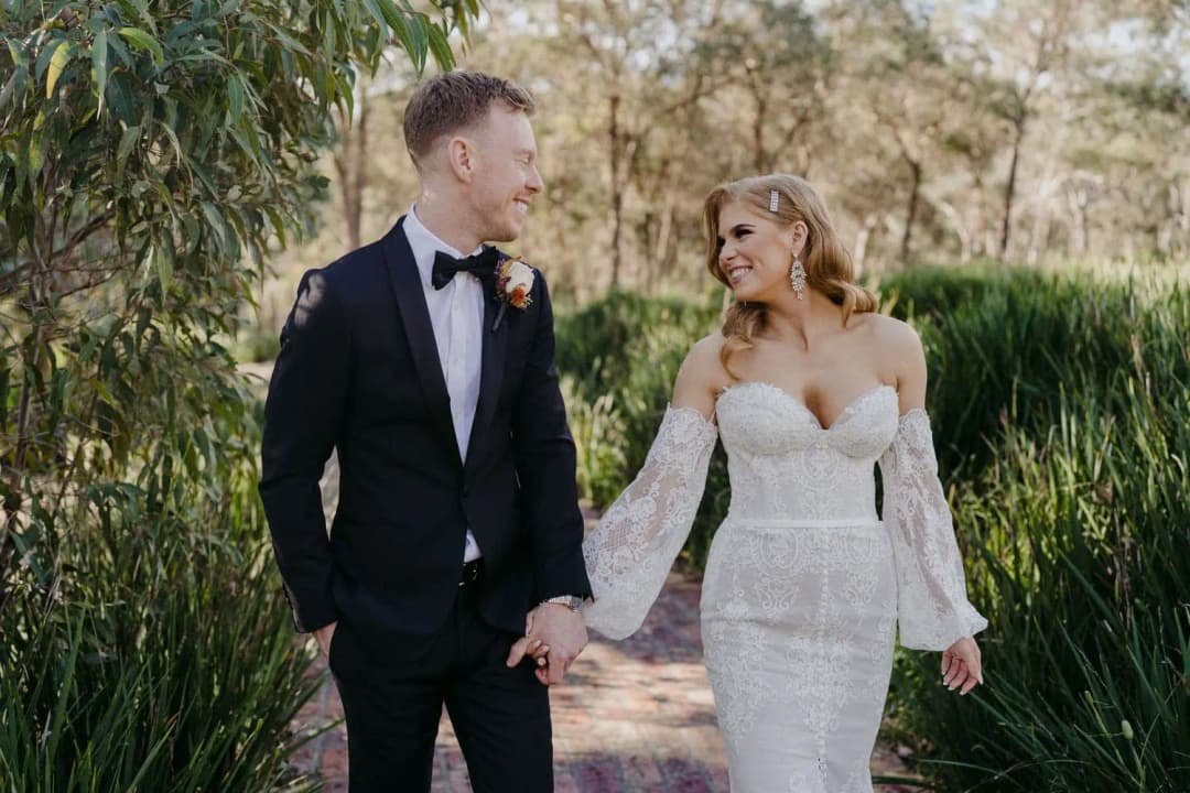 Bride and groom holding hands as they walk along a garden path