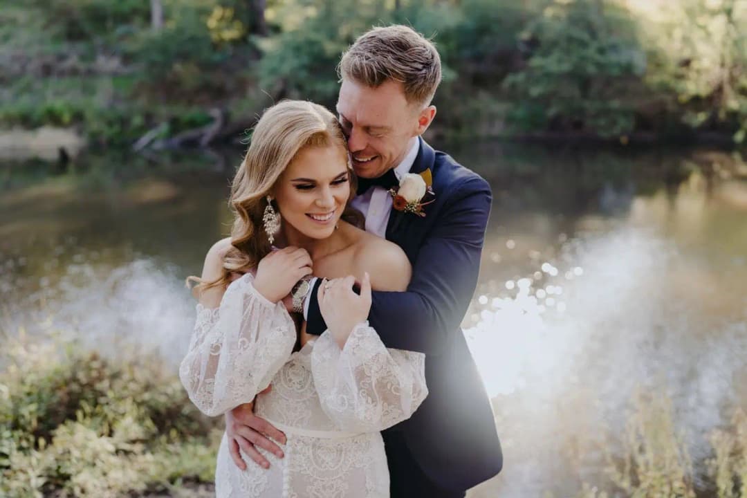 Groom embracing the bride from behind beside a garden pond