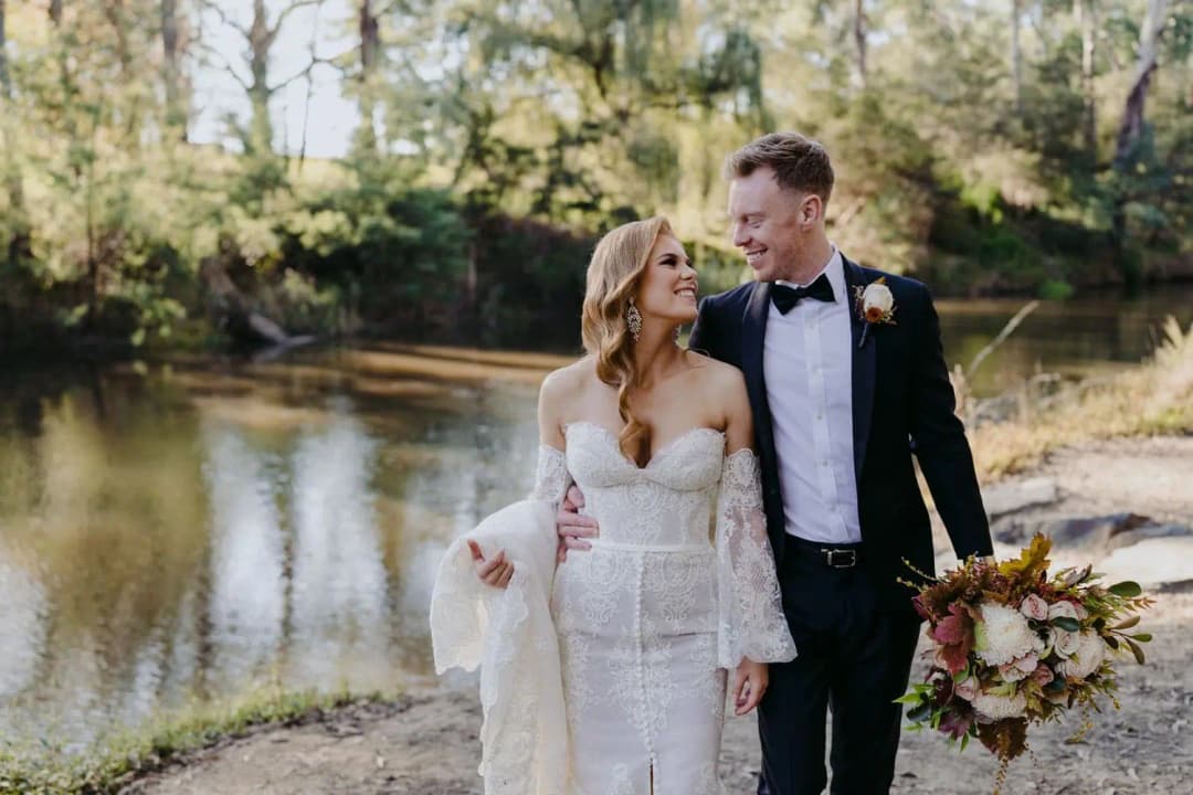 Newlyweds smiling while standing together beside a pond