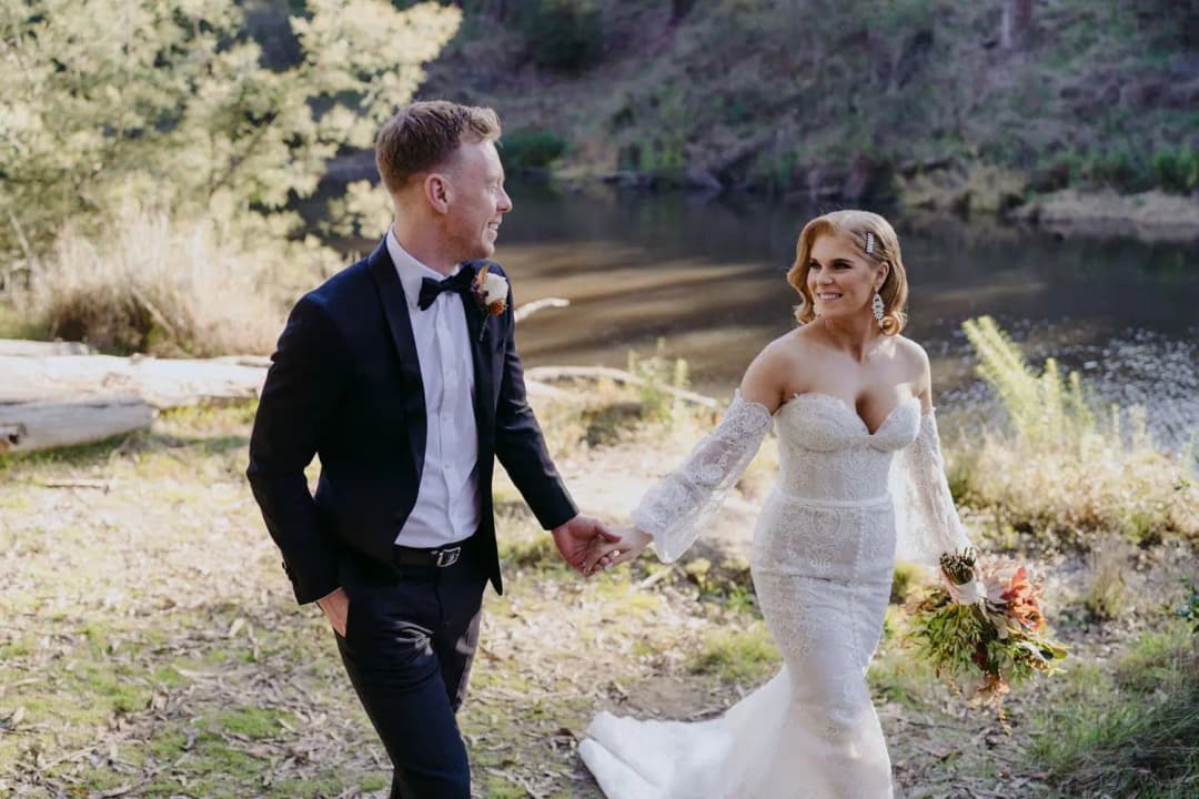 Groom leading the smiling bride by the hand beside the pond
