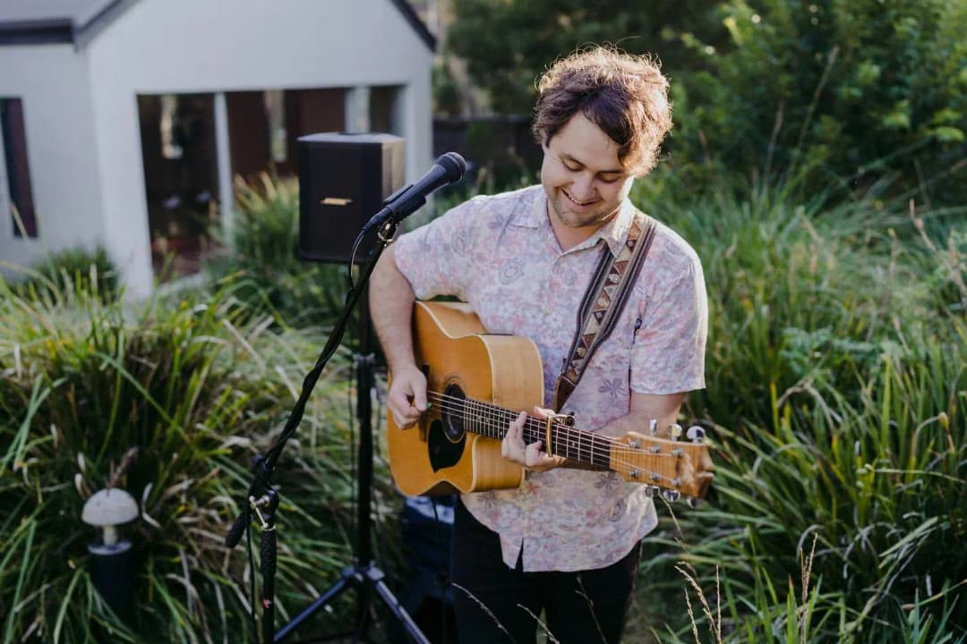 Musician playing an acoustic guitar beside a microphone in the garden