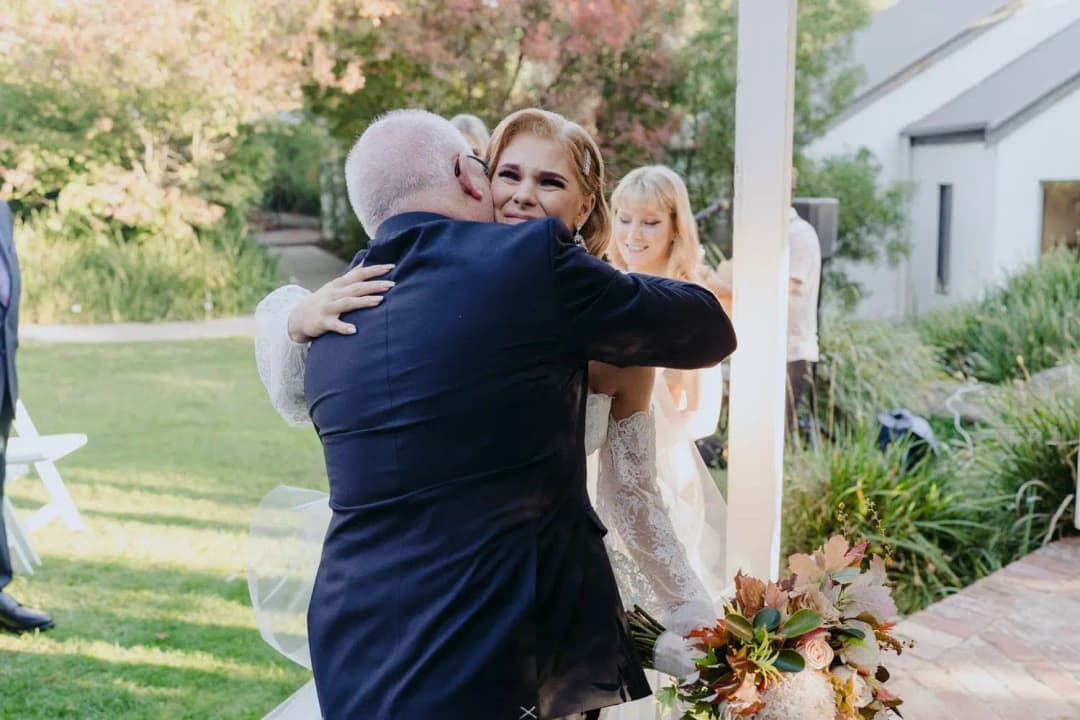 Bride embracing an older man beside the ceremony gazebo