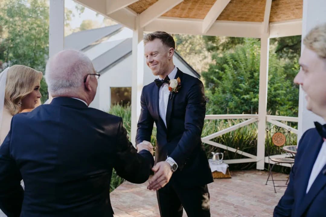 Groom greeting an older man with a handshake at the gazebo