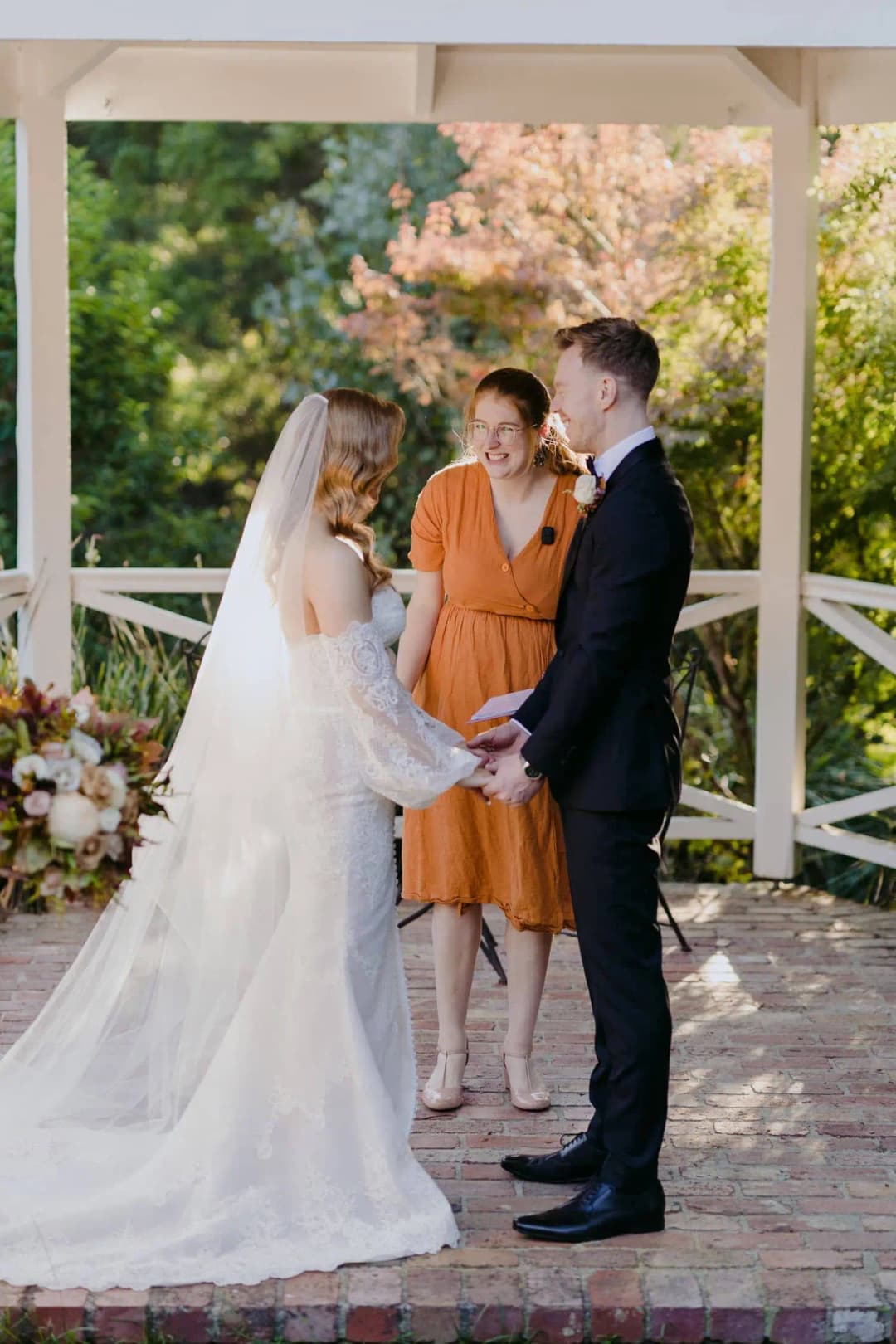 Bride and groom facing each other with a celebrant inside a gazebo