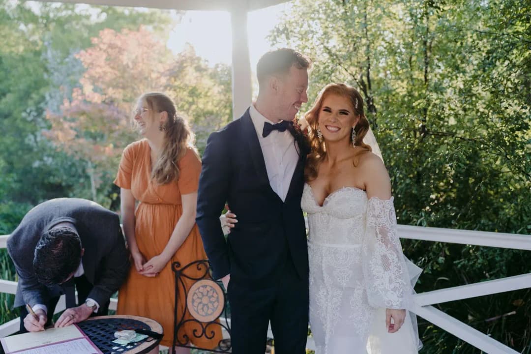 Newlyweds smiling together as the groom signs the wedding register