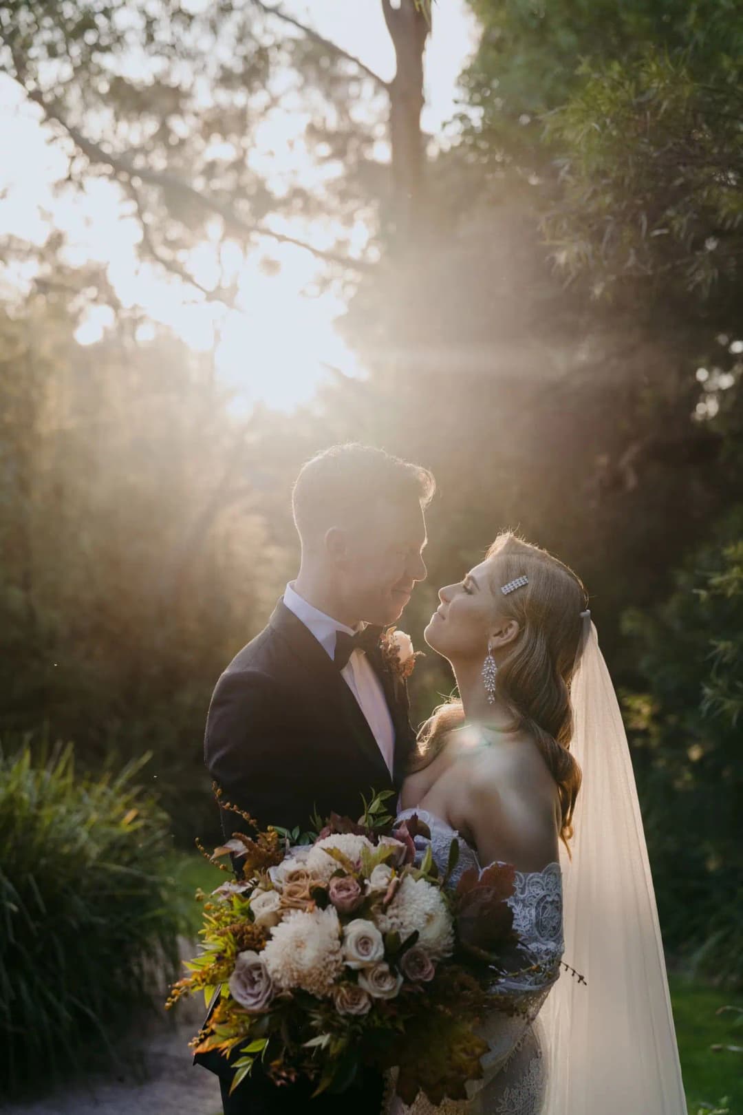 Bride and groom kissing beneath sunlight filtering through trees