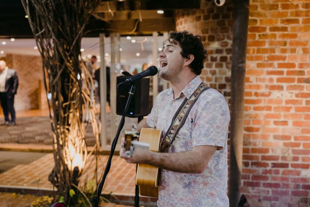 Musician singing into a microphone while playing an acoustic guitar indoors