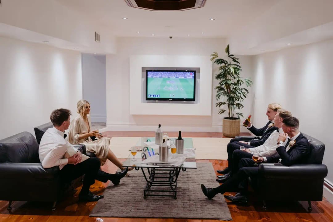 Wedding party seated around a coffee table watching a television