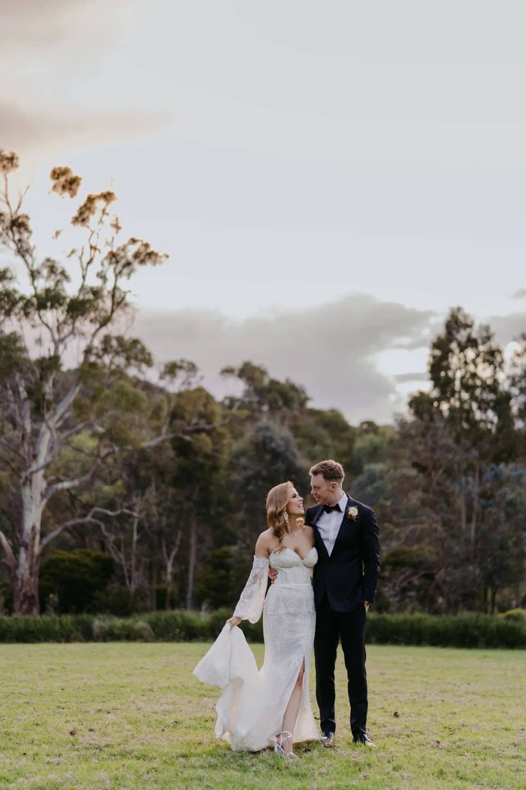 Bride and groom standing together on a lawn with hills behind them