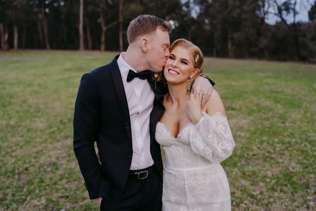 Groom kissing the smiling bride on the cheek outdoors