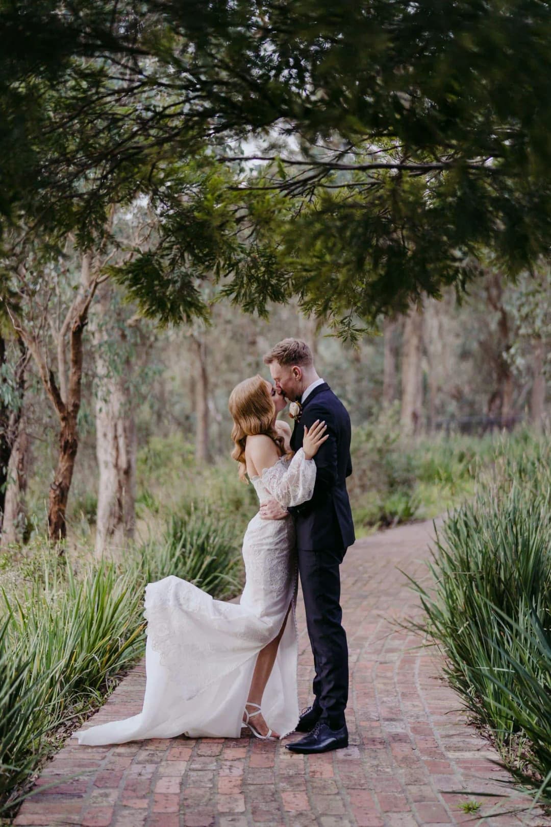 Bride and groom embracing beside tall garden trees
