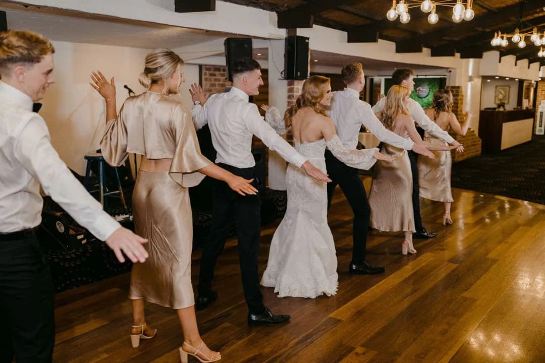 Wedding party dancing together in a line beneath reception lights