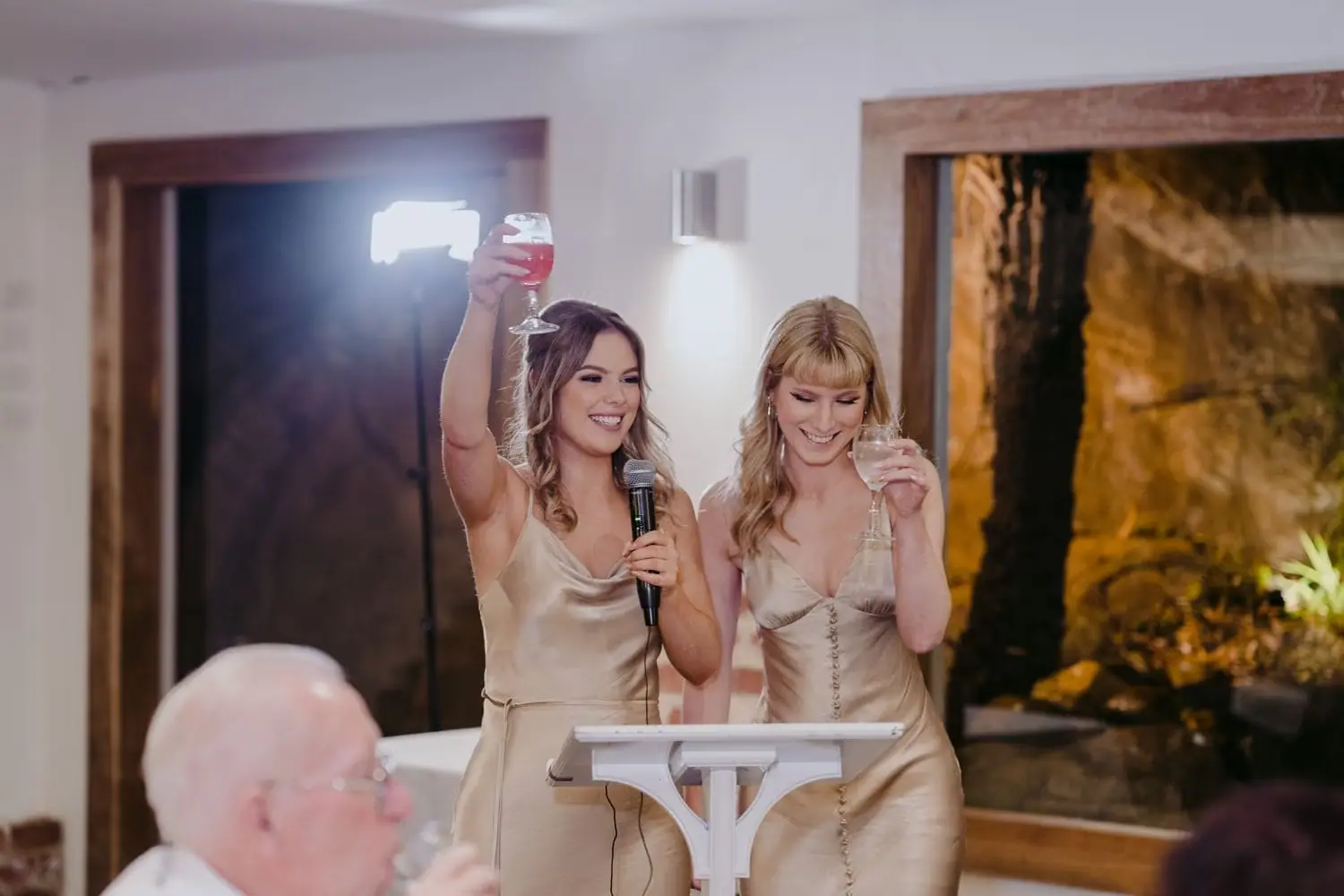 Two bridesmaids standing together with a microphone and a raised phone