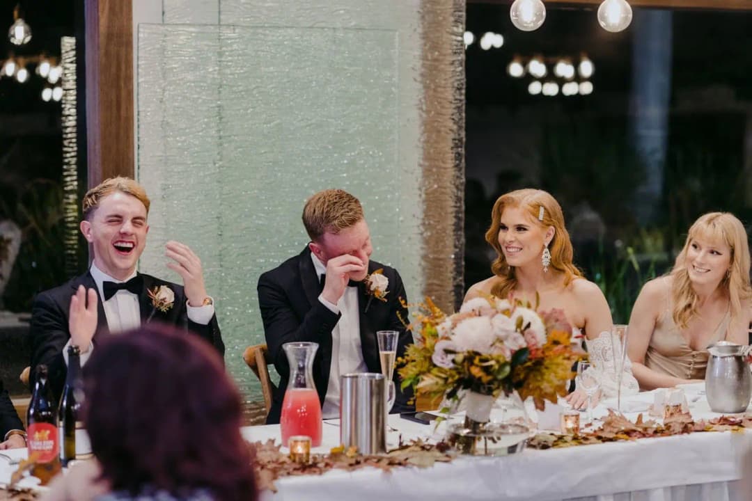 Wedding party laughing together while seated at the reception table