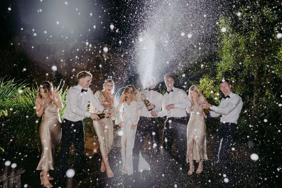 Wedding party cheering beneath spraying sparkling wine outdoors at night