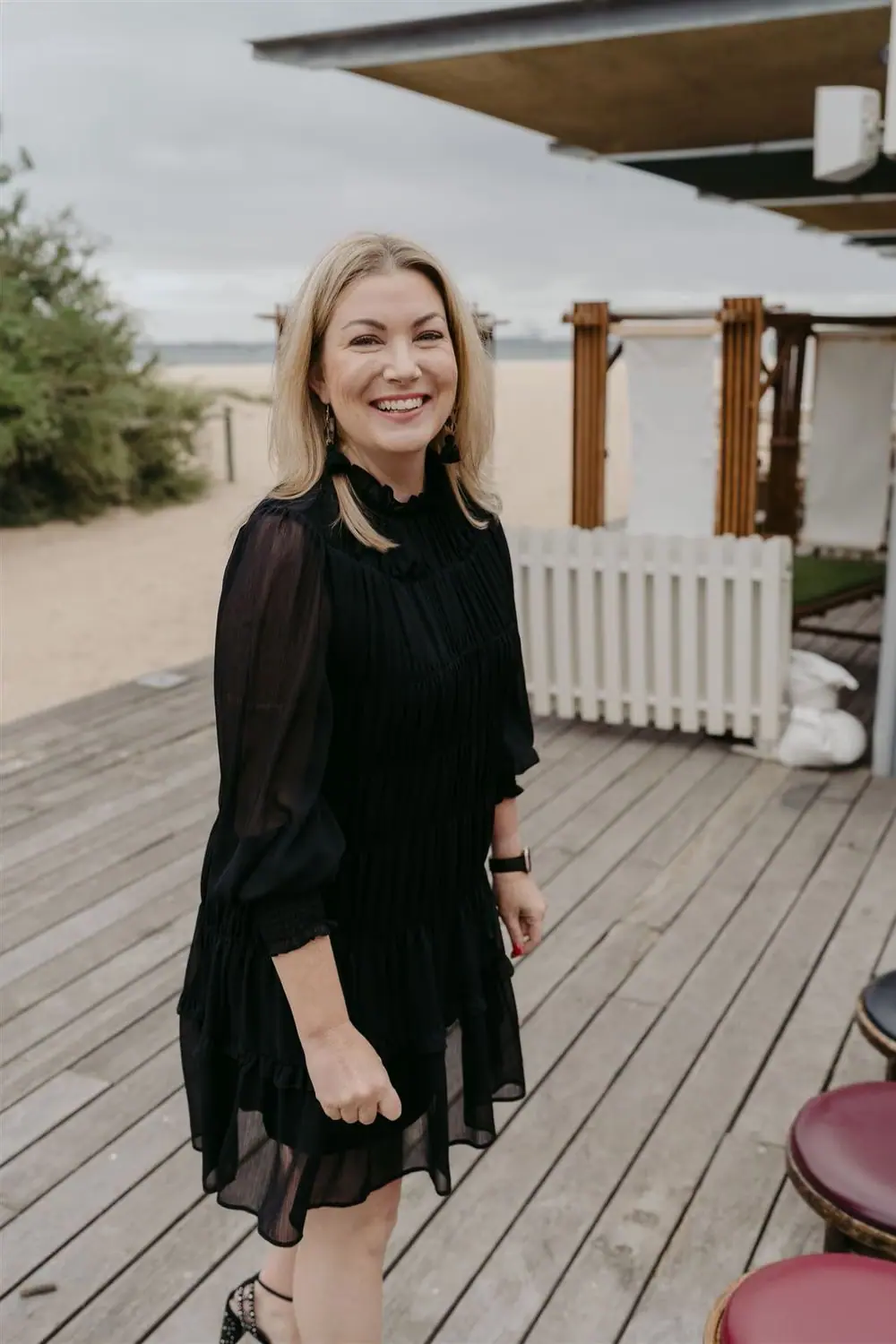 Woman in a black dress smiling on an outdoor deck.