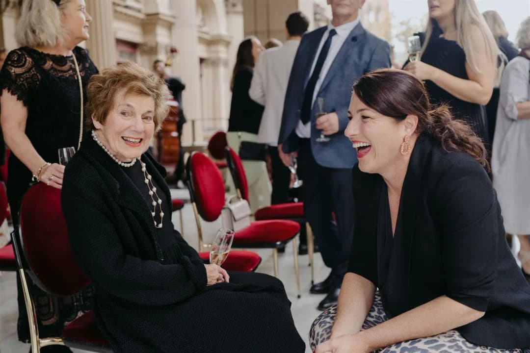 Woman laughing with an older seated guest after a ceremony.