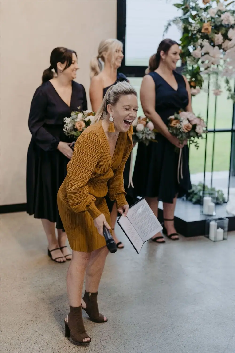 Woman laughing with companions beside an indoor ceremony.