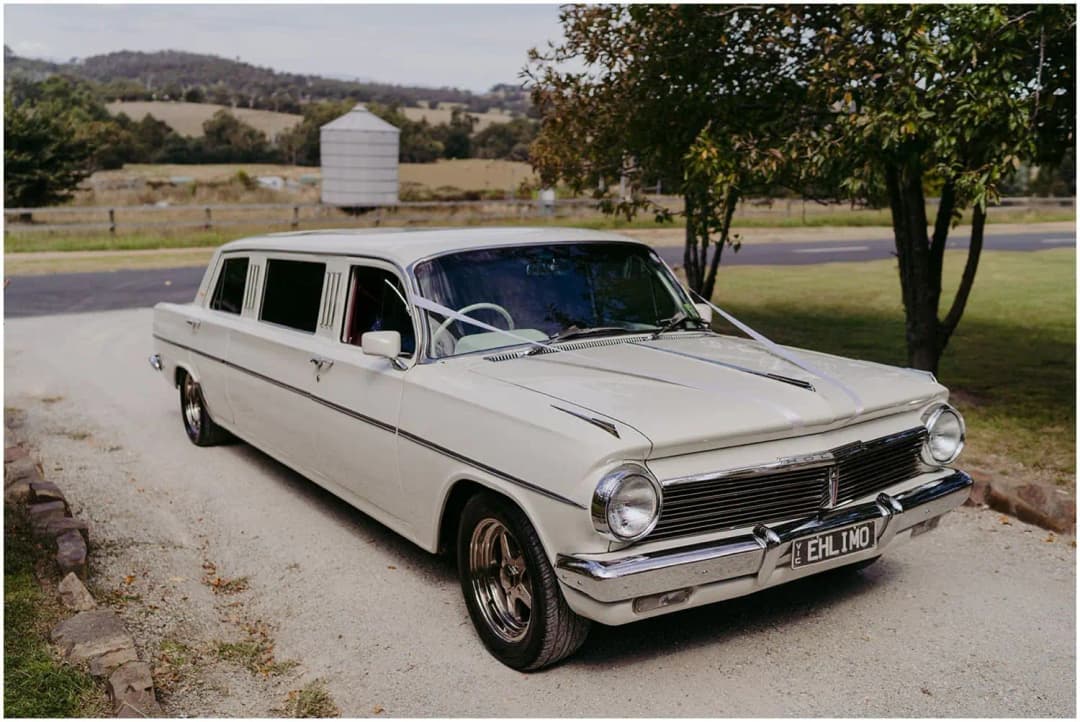 White vintage limousine parked beside farmland and distant hills