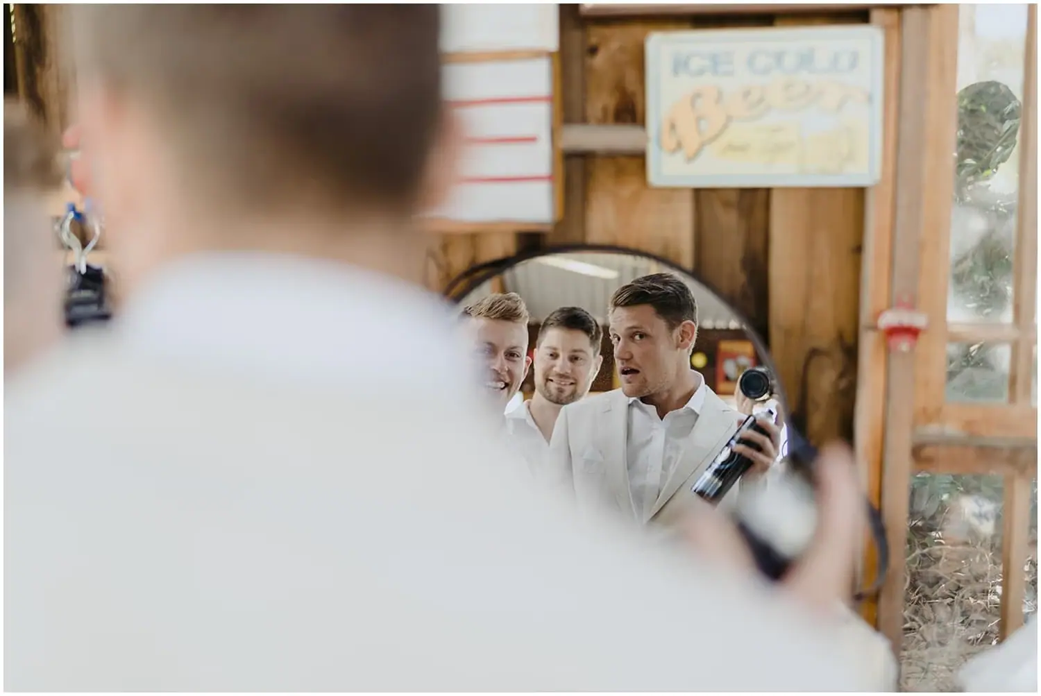 Men laughing together in a mirror while getting ready in a rustic room