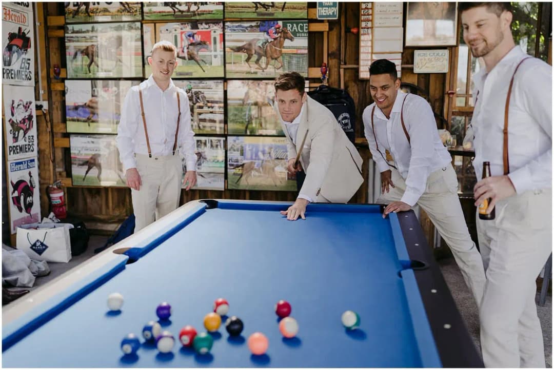 Men in pale suits playing pool in a room decorated with posters