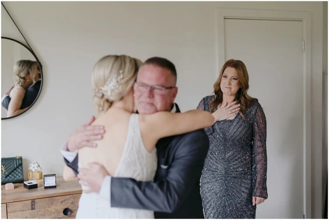 Bride hugging a man in a dark suit while a woman watches