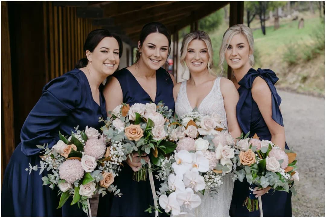 Bride and three bridesmaids in navy dresses posing together with bouquets