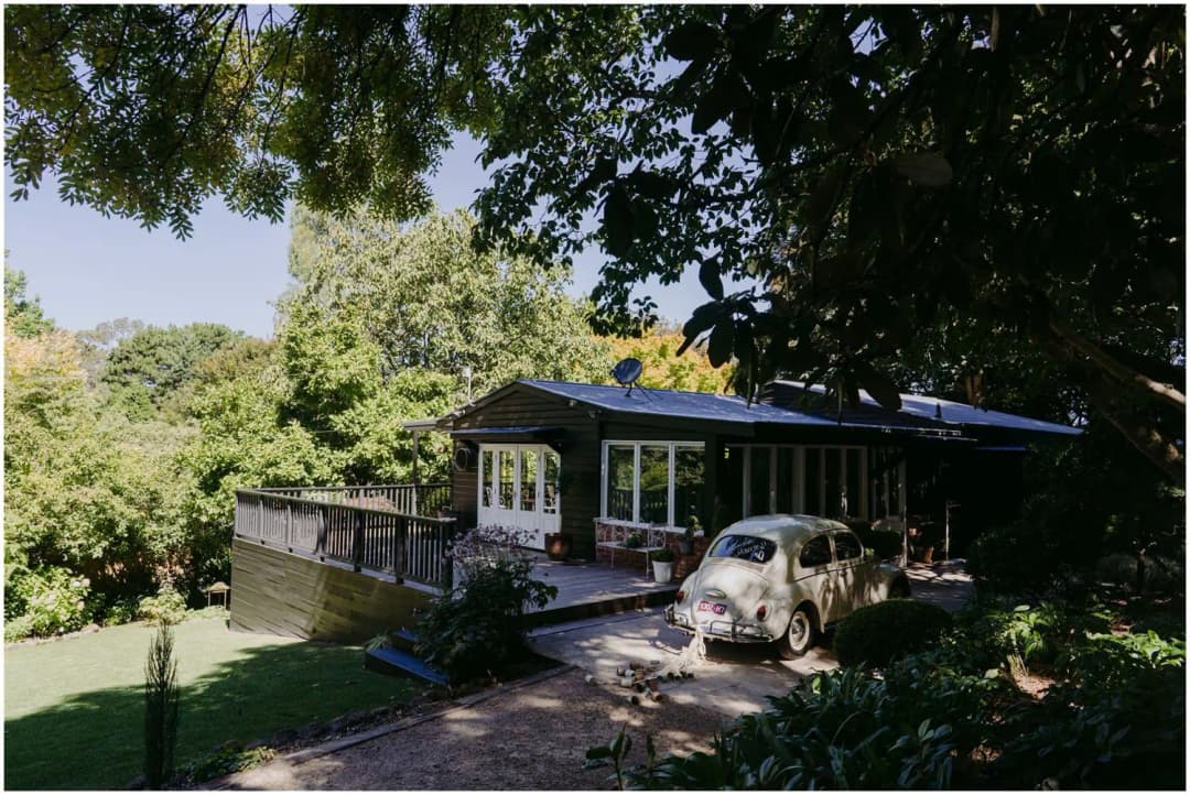 Dark cottage and white vintage car surrounded by a leafy garden