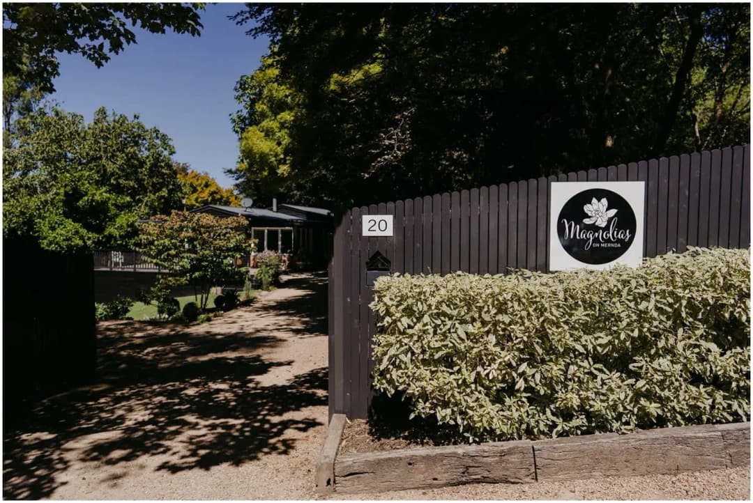 Shaded driveway entrance with a timber fence, a number 20 plaque and leafy trees