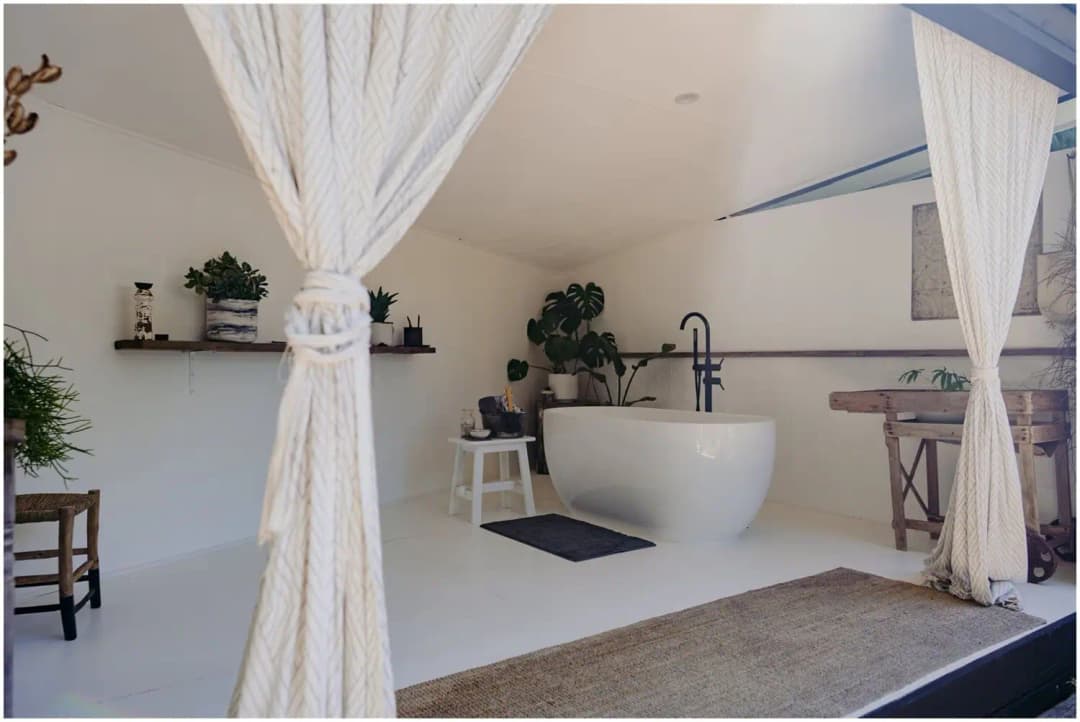 Freestanding white bath on a raised platform framed by pale curtains