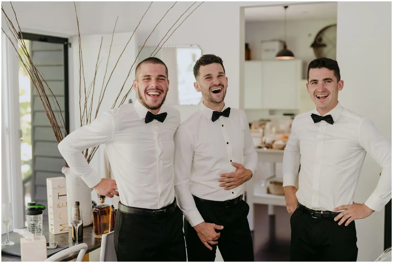 Three men laughing together in white shirts and black bow ties