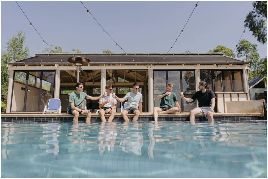 Five friends sitting beside a swimming pool with their arms linked