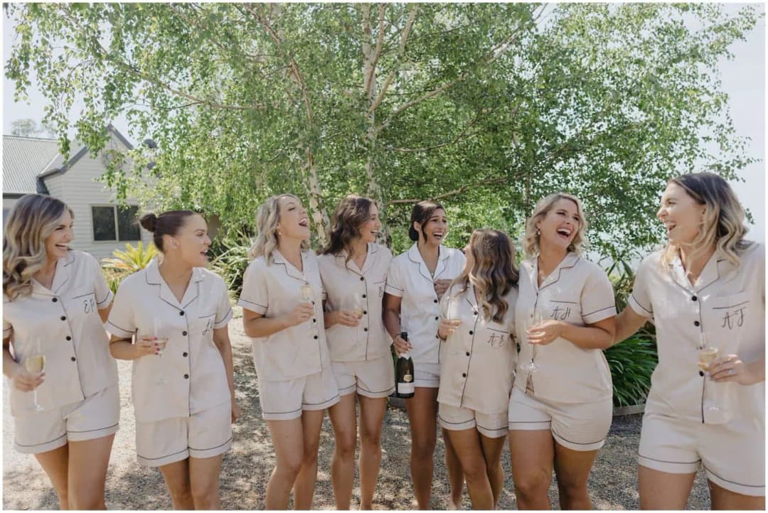 Women laughing outdoors in pale matching sleepwear while holding drinks