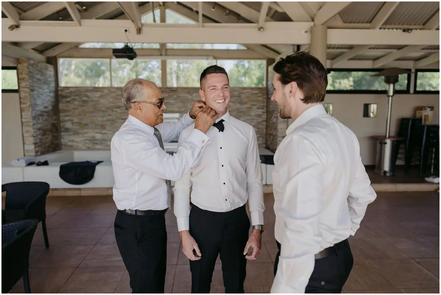 Man adjusting the groom's bow tie while a friend watches