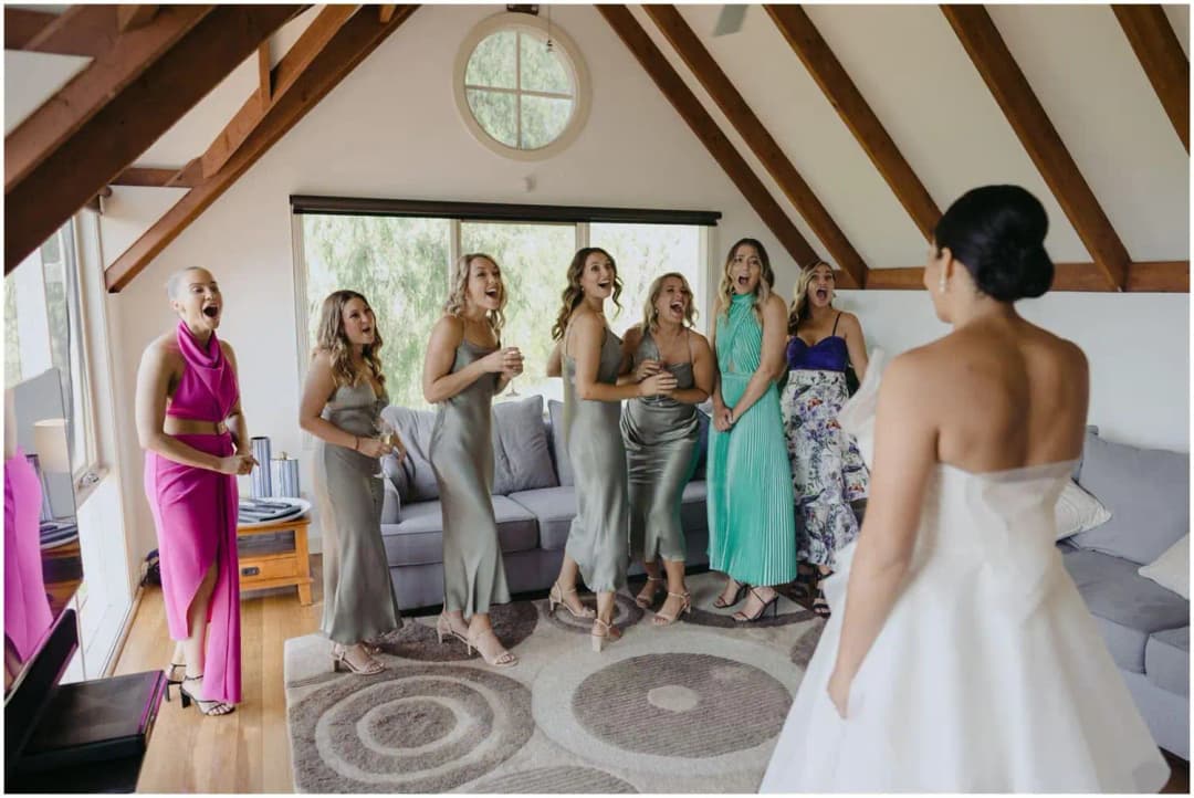 Bride facing smiling friends in an upstairs room with exposed timber beams