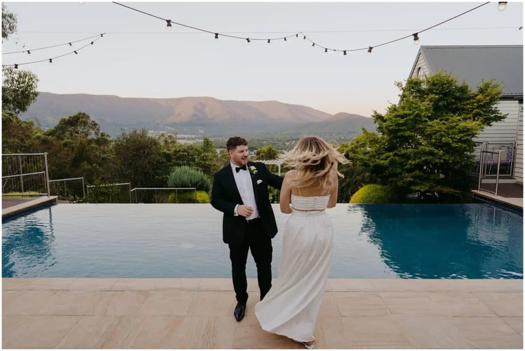 Bride turning toward the groom beside an infinity pool under festoon lights