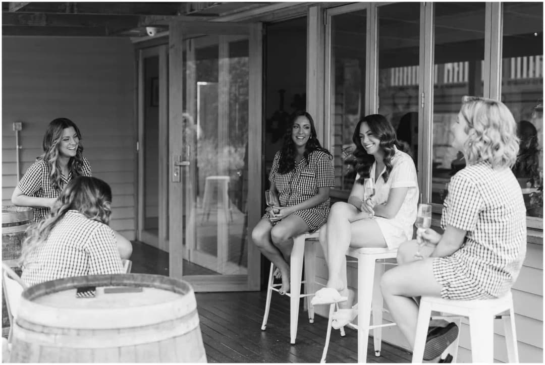 Black and white photograph of women chatting on stools beside timber verandas