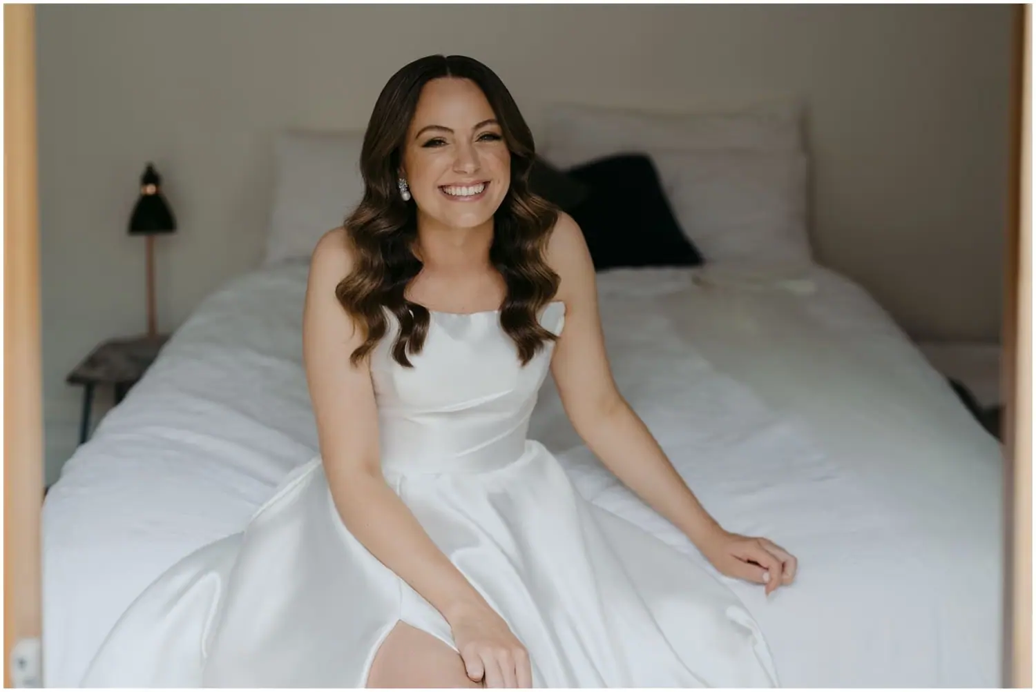 Bride smiling while seated on a bed in her wedding dress