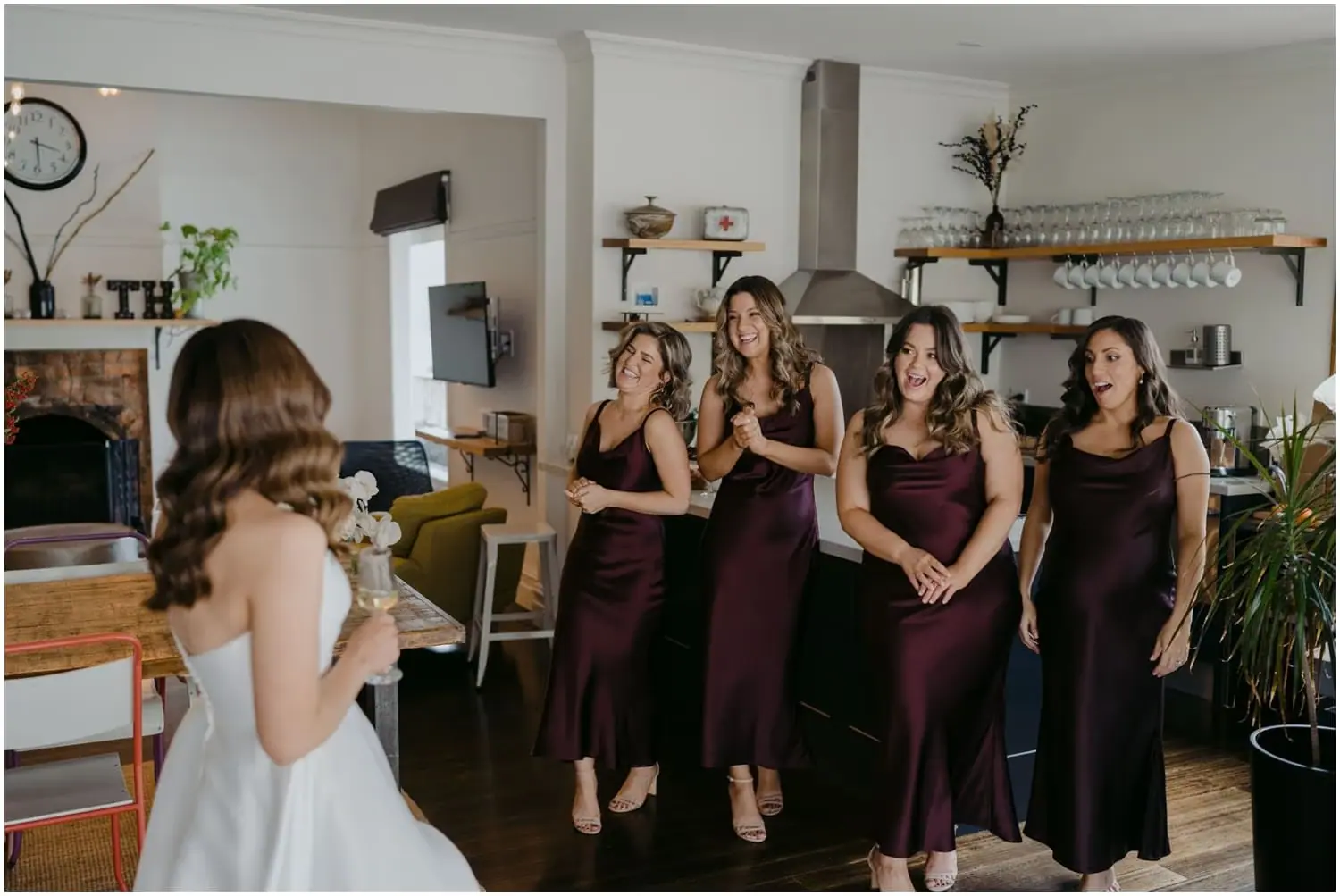 Bride facing four smiling bridesmaids in burgundy dresses indoors