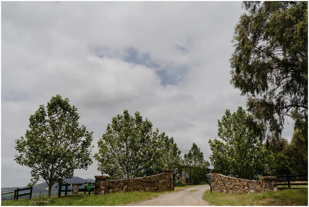 Gravel driveway passing between stone walls beneath a cloudy sky