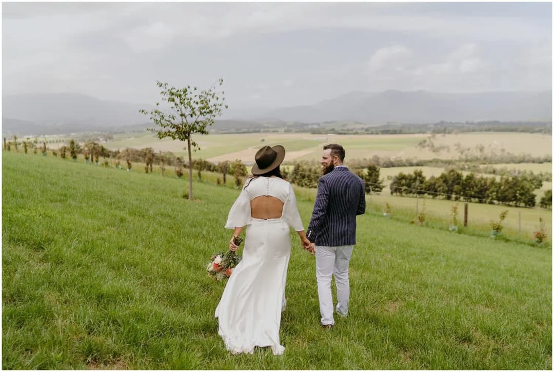 Bride and groom walking across a grassy slope overlooking a valley