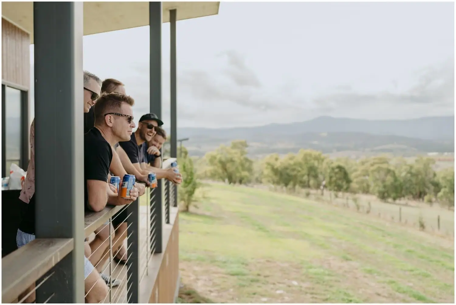 Men leaning on a covered balcony railing overlooking farmland and hills