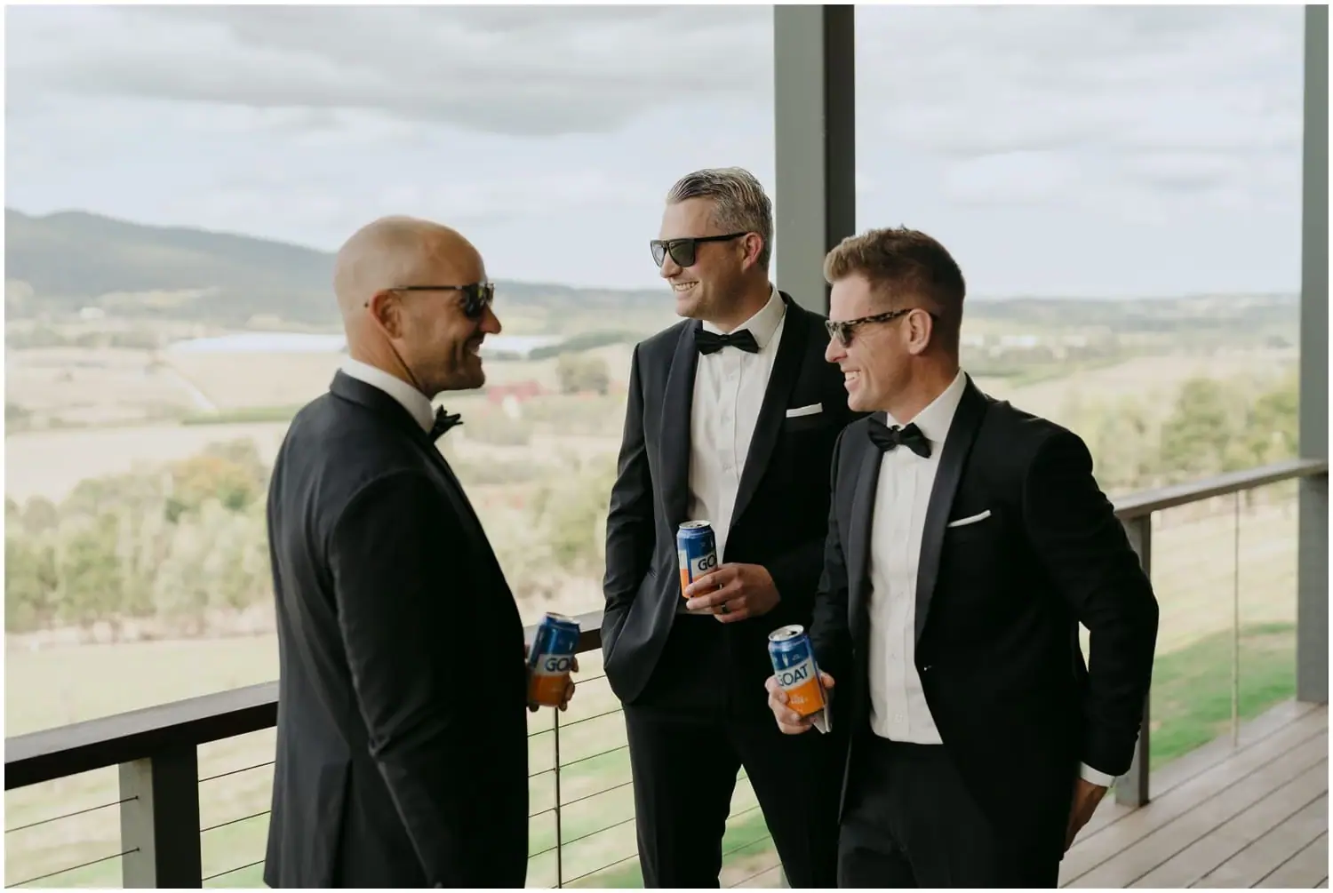 Three men chatting in black suits and bow ties while holding drinks