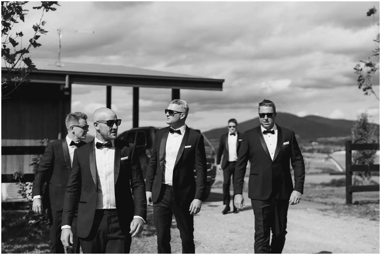 Black and white photograph of men walking outdoors in suits and sunglasses