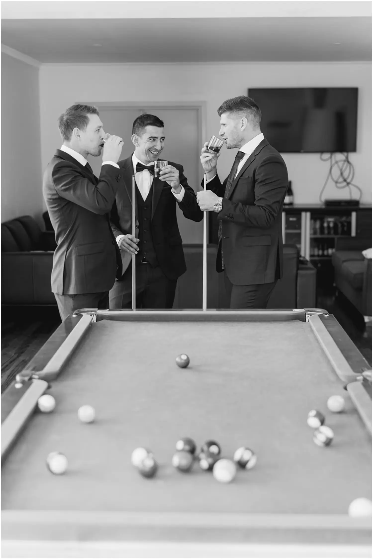 Black and white photograph of three men drinking and laughing beside a pool table