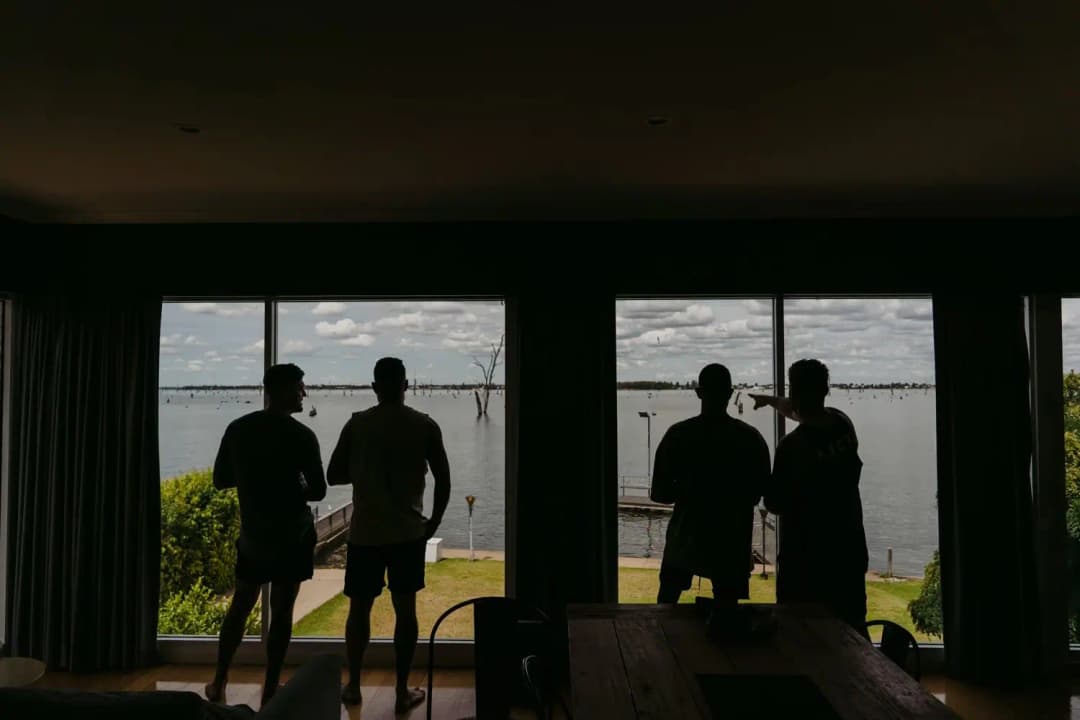 Silhouettes of four men standing indoors in front of windows overlooking a lake
